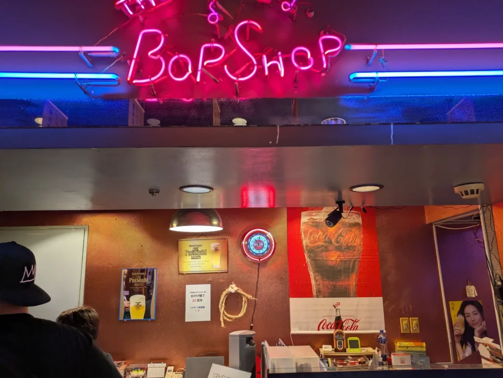 バイキング居酒屋リオの店内にある、ピンクとブルーの鮮やかな「Bar Shop」のネオンサインとカウンター